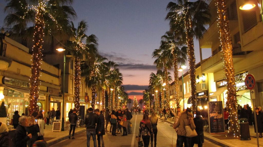 Forte dei Marmi, oltre l’estate: vivere la Versilia come un vero local 3 Via del centro di Forte dei Marmi illuminata con luci natalizie tra palme e negozi, con molte persone che passeggiano durante le festività serali.