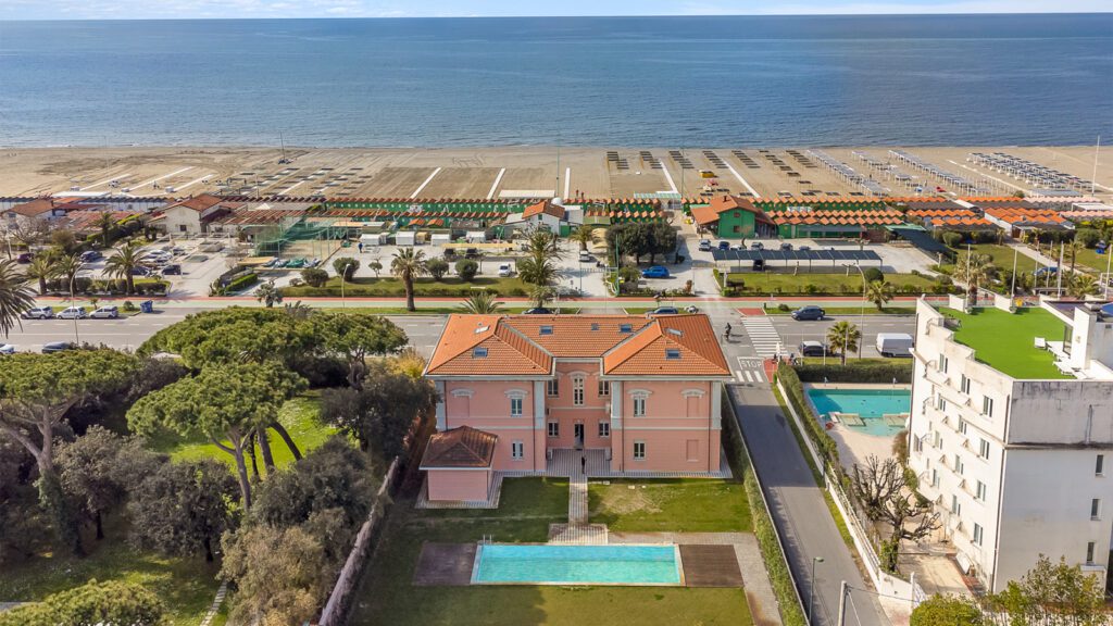 Vendita case Forte dei Marmi: tendenze e desideri degli acquirenti di immobili di prestigio 3 Villa storica color rosa con piscina privata a Forte dei Marmi, vista dall’alto con il mare e gli stabilimenti balneari sullo sfondo.