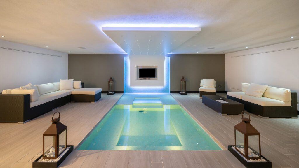 Vendita case Forte dei Marmi: tendenze e desideri degli acquirenti di immobili di prestigio 4 Piscina interna di una villa di lusso a Forte dei Marmi con illuminazione moderna, area relax con divani e lanterne decorative.