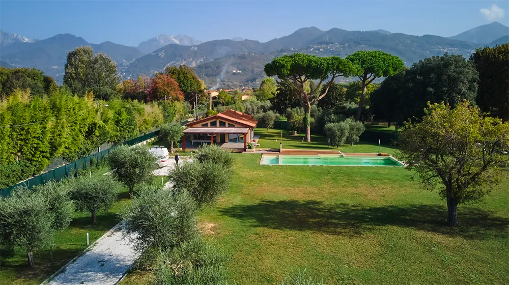 Vista panoramica di una villa a Pietrasanta con ampio giardino, piscina e alberi secolari. Il paesaggio montano sullo sfondo crea un'atmosfera serena e naturale, ideale per una residenza immersa nel verde.