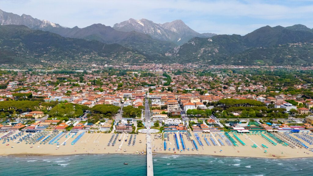 Panoramica dall’alto di Forte dei Marmi: il litorale della Versilia, il pontile iconico, le eleganti residenze e lo sfondo delle Alpi Apuane.